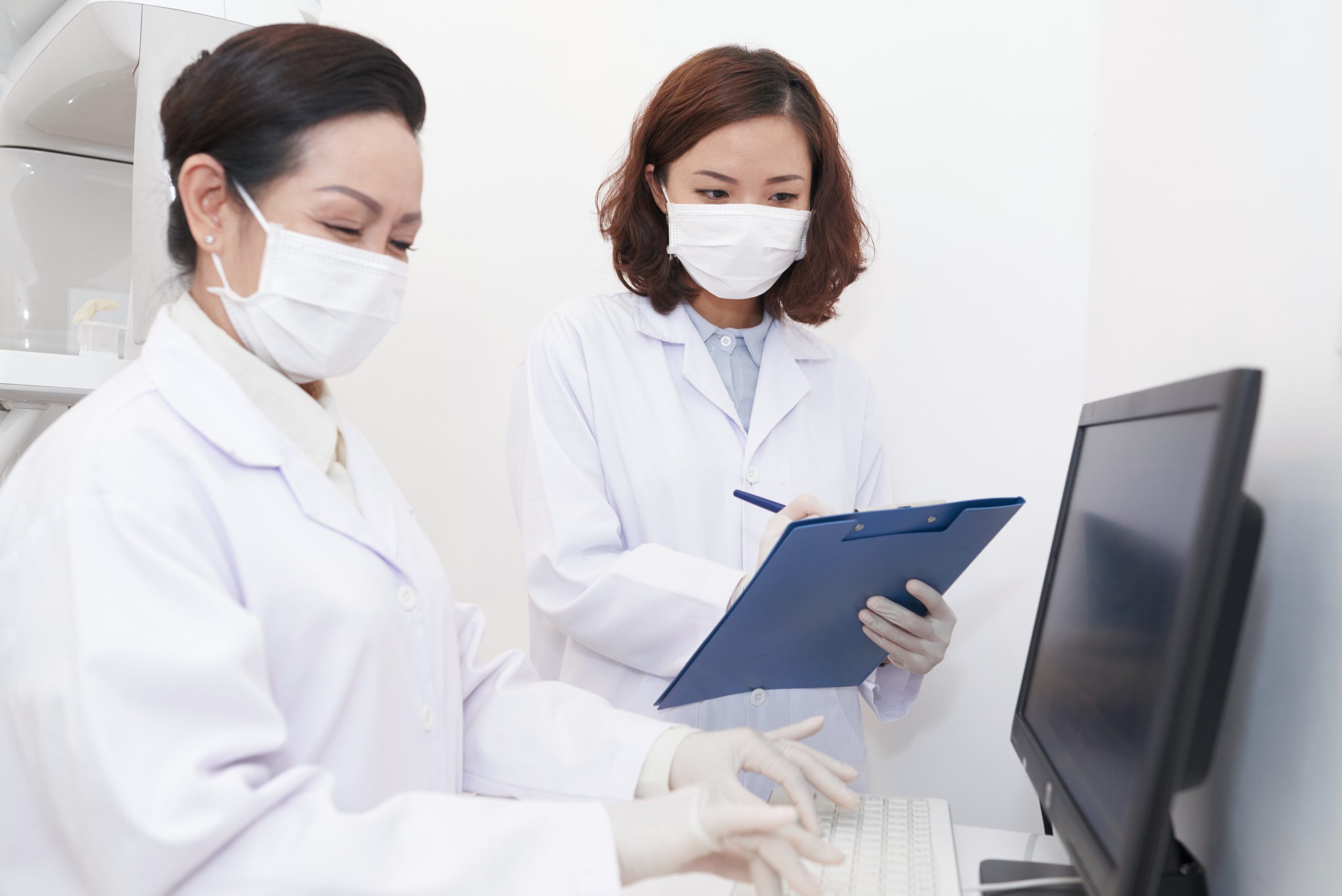Dentist reading medical record aloud and nurse entering information in computer